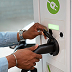 Person plugging an electric vehicle charger into a white charging station with a green recycling symbol.