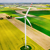 Aerial view of a large white wind turbine standing in the middle of vibrant green and yellow agricultural fields.