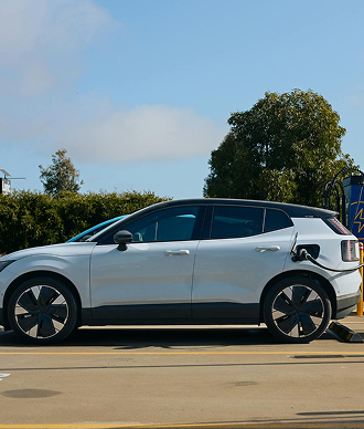 Silver electric SUV charging at a station under blue sky with trees in the background.