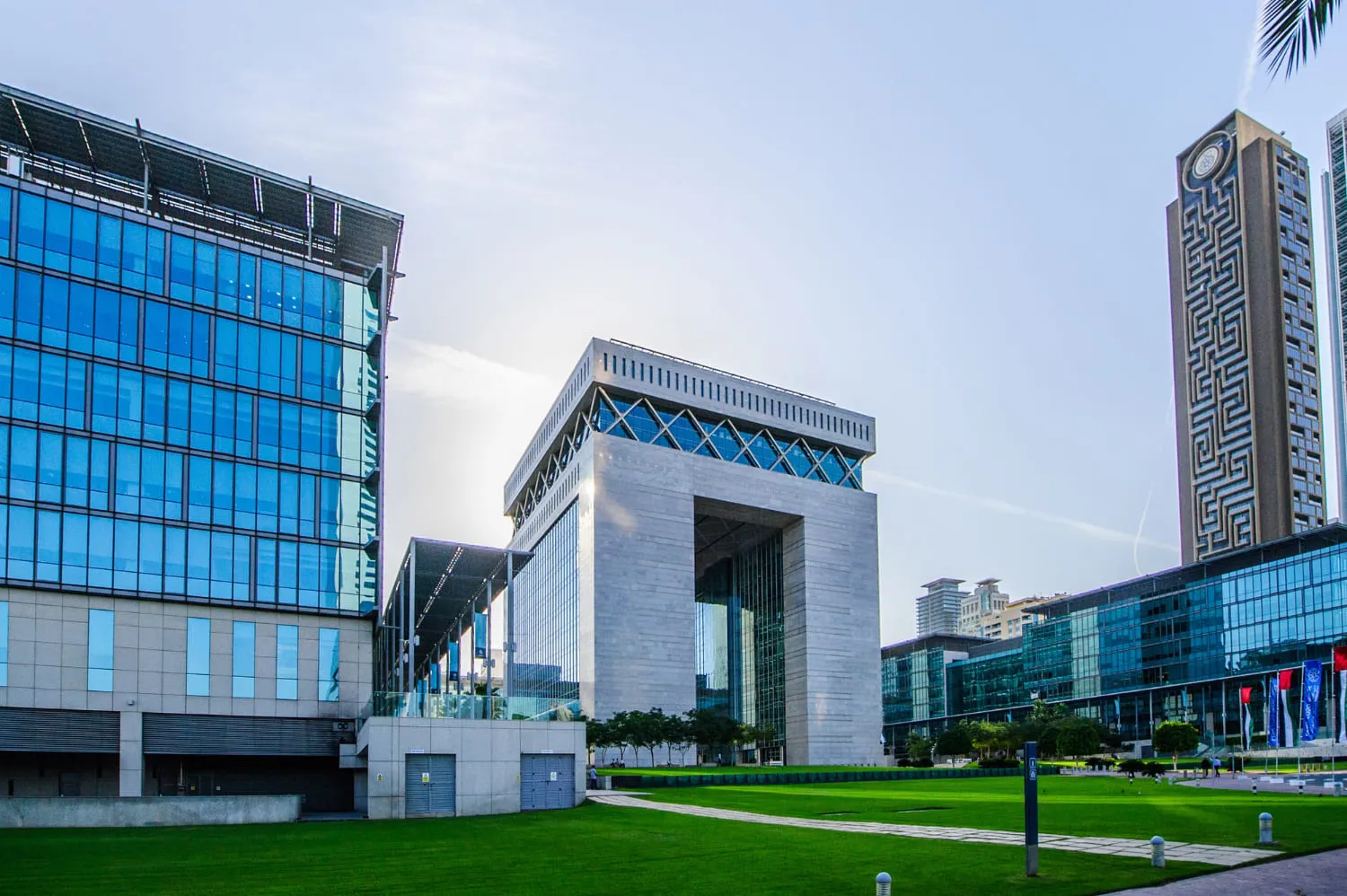 Modern buildings with glass facades surrounding a large green lawn under a clear blue sky.