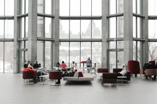 People sitting and conversing in a spacious modern building lobby with large windows showing a snowy cityscape outside.
