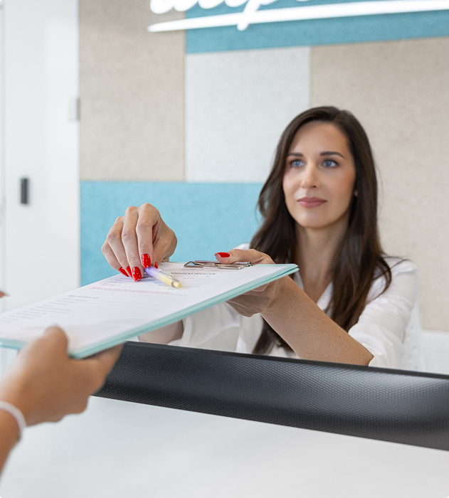 Žena za recepcí podává formulář s propiskou návštěvníkovi.