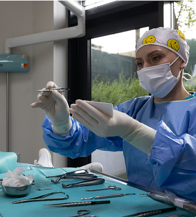 Zdravotní sestra v modrém ochranném oblečení a roušce připravuje chirurgické nástroje v zdravotnickém zařízení.