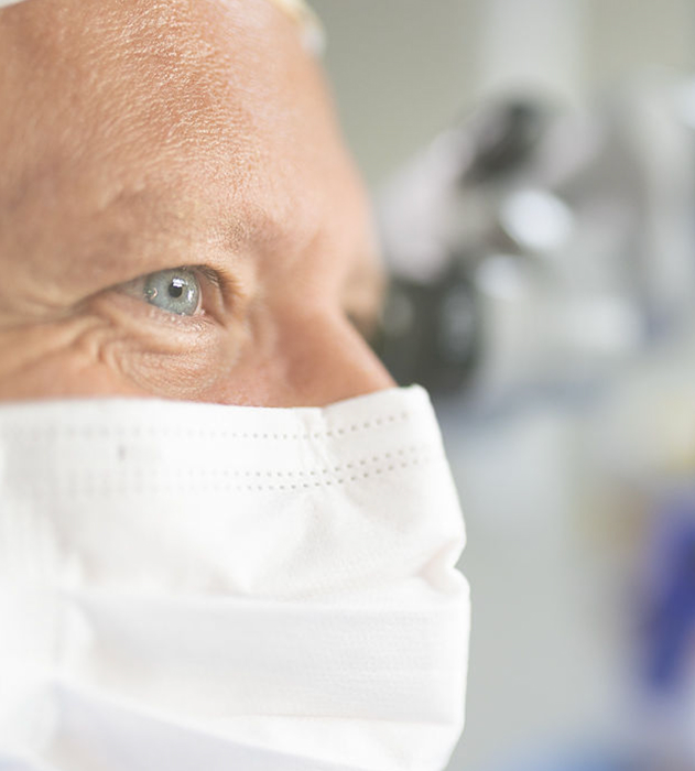 Detailní záběr na osobu s modrýma očima nosící bílý lékařský respirátor.