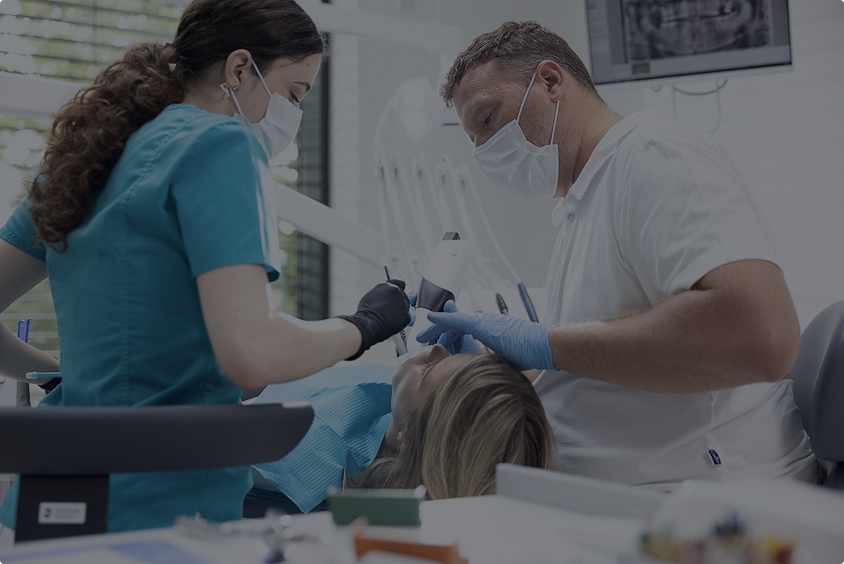 Zubař a zdravotní sestra ošetřují pacientku na zubním křesle v ordinaci.