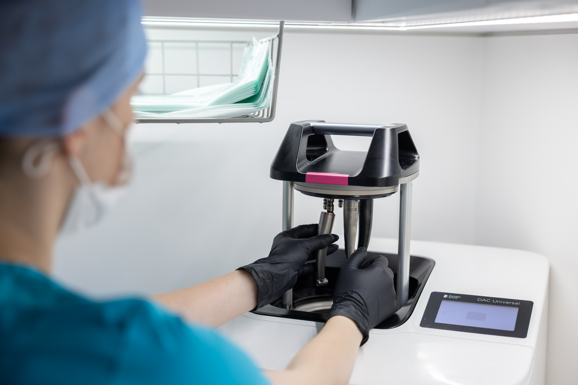 Zdravotnický pracovník v ochranné čepici a rukavicích manipuluje s lékařským zařízením DAC Universal v sterilním prostředí.