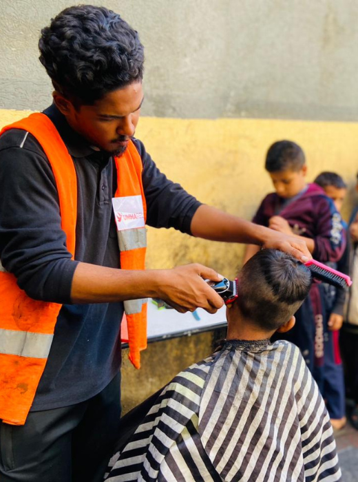 Umma Relief volunteer offering a free haircut to a child in Gaza, restoring dignity and care through the Trucks of Hope initiative.