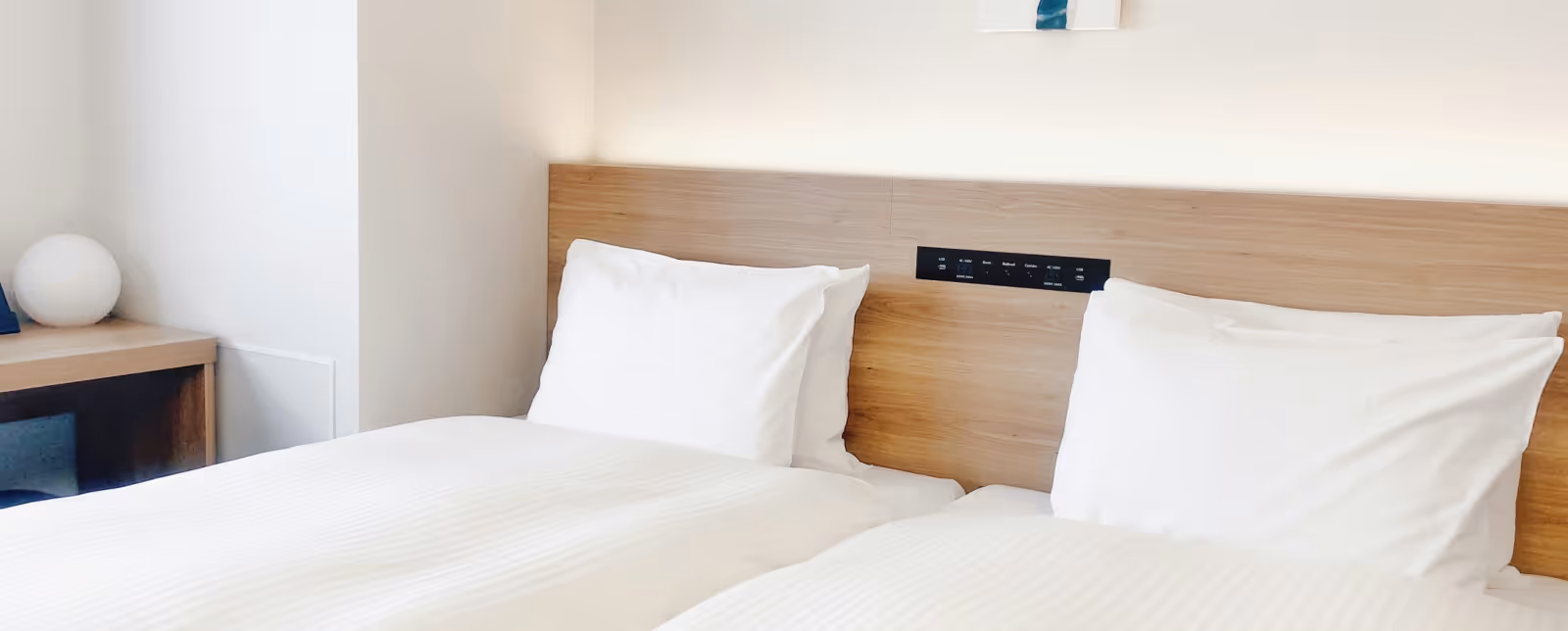 Twee eenpersoonsbedden met witte lakens en kussens in een moderne hotelkamer met houten hoofdeinden en een nachtkastje.