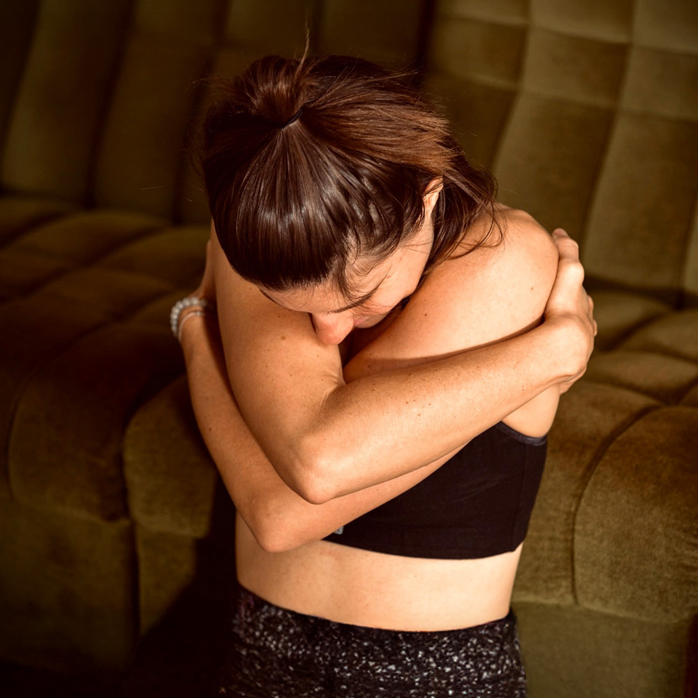 Person sitzt ruhig und umarmt sich selbst in einer Geste von Nähe und Selbstzuwendung.