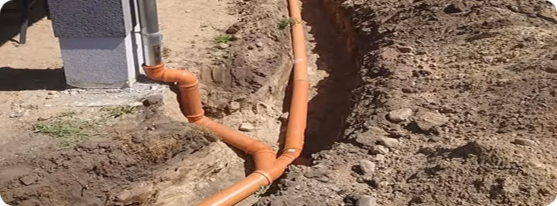 Im Boden verlegte orangene Abflussrohre neben einem Hausgrundstück.