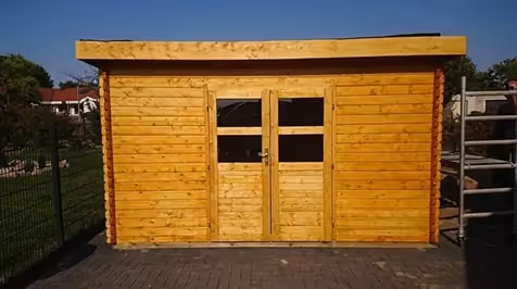Kleines Gartenhaus aus Holz mit Doppeltür und Fenstern unter klarem blauem Himmel.