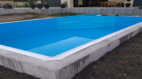 Leerer blauer rechteckiger Pool in einem teilweise fertigen Außenbereich.