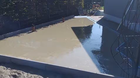 Frisch gegossene Betonfläche in rechteckiger Form im Freien mit Schatten und umgebender Bauumgebung.