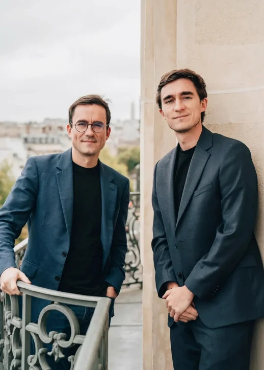 Réunion d'affaires avec cinq personnes assises autour d'une table en bois dans une salle lumineuse aux grandes fenêtres.