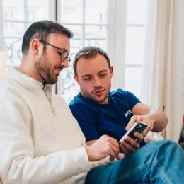 Groupe de cinq personnes en tenue professionnelle discutant autour d'une table avec ordinateurs portables en réunion.