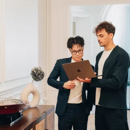 Deux jeunes professionnels en tenue décontractée collaborent en regardant un ordinateur portable dans un bureau moderne.