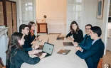 Groupe de cinq jeunes professionnels en réunion dans une salle de conférence, avec un ordinateur portable et des documents sur la table.