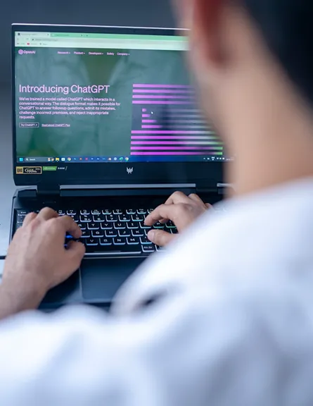 Personne tapant sur un ordinateur portable affichant la page d'accueil de ChatGPT en anglais.