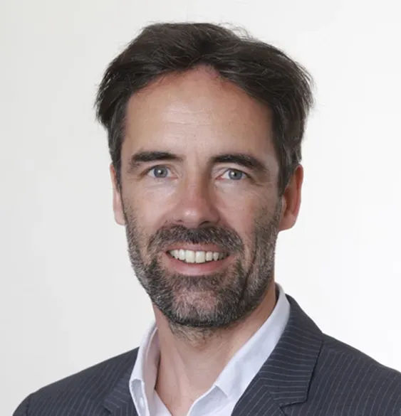 Un homme présente des graphiques financiers sur un grand écran tactile à deux collègues qui prennent des notes sur tablette et cahier dans un bureau moderne.