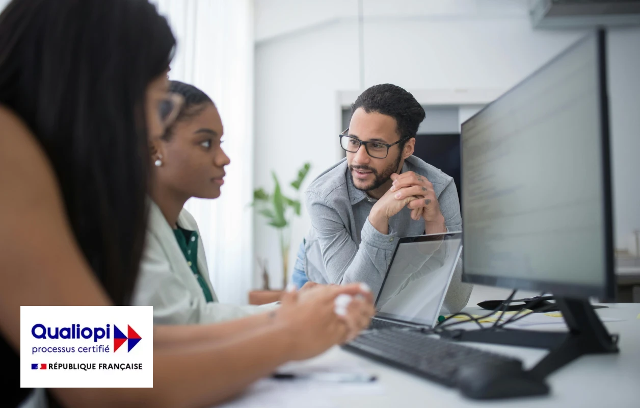 Trois personnes en réunion dans un bureau, regardant un grand écran d'ordinateur sur un bureau.
