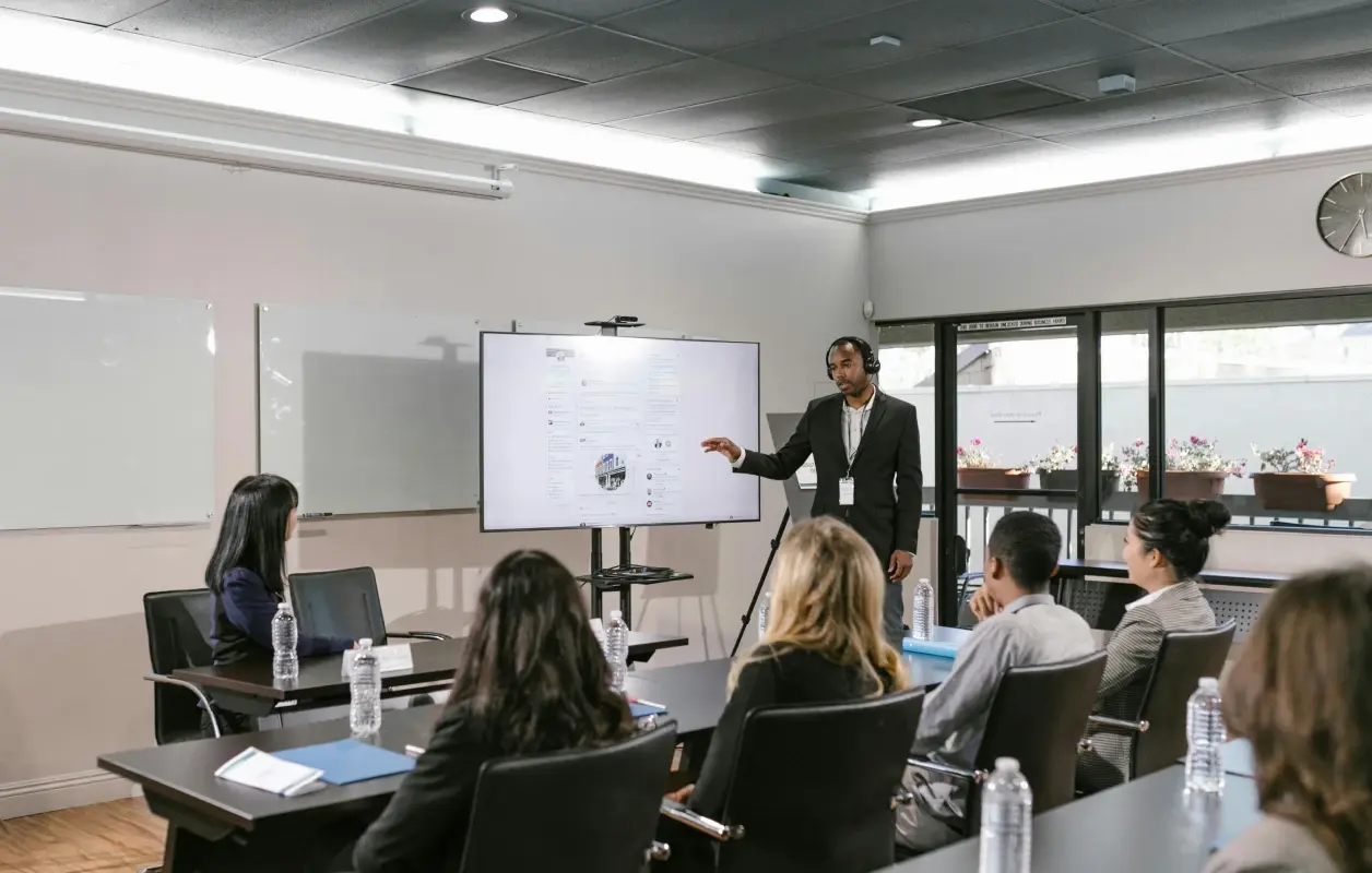 Homme portant une veste bleue sombre et un col roulé noir, tenant un microphone et parlant en faisant un geste de la main.
