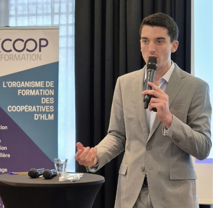 Un homme en costume bleu tenant un microphone et parlant lors d'une interview ou d'une discussion.