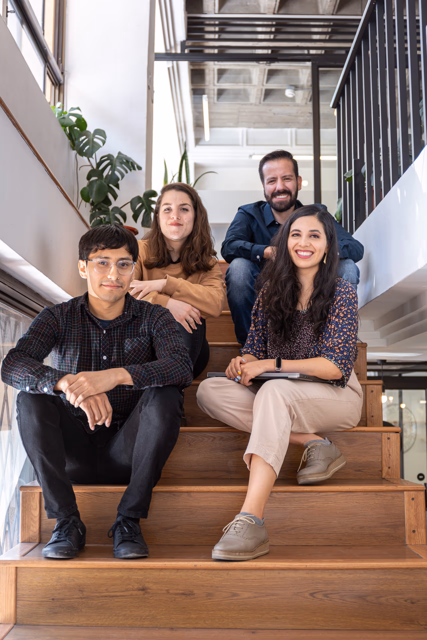 Four team members sitting on wooden stairs in a bright office, smiling at the camera.