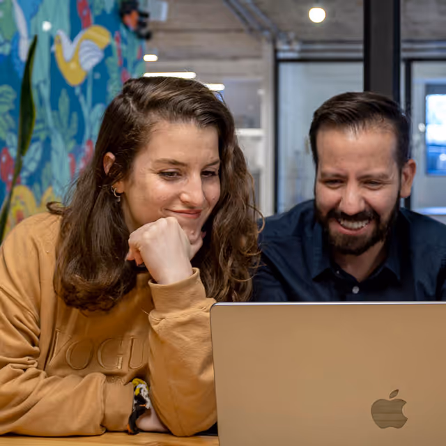 A woman and a man smiling while looking at a laptop together in a colorful office space.