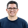 Smiling man with glasses wearing a dark blue sweater against a white background. Harry Cruz Rhesis