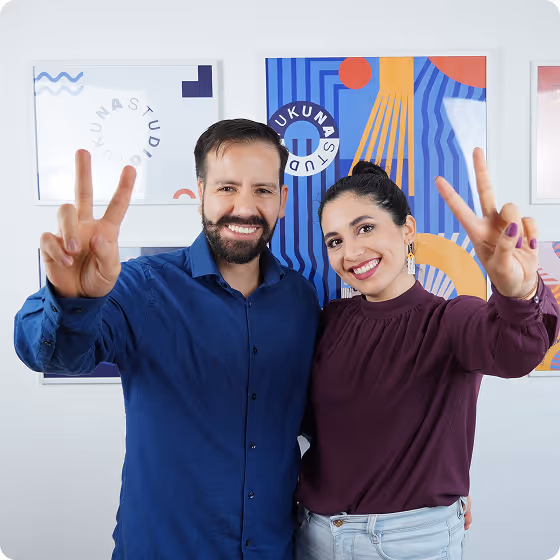 Smiling man and woman standing side by side showing peace signs with both hands in front of colorful abstract artwork.