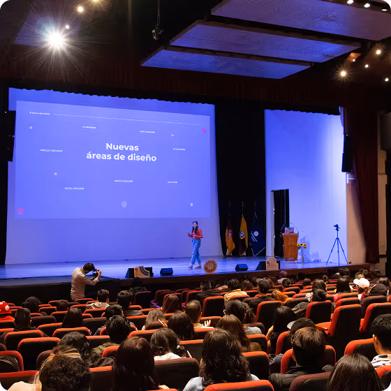 Speaker presenting on stage in front of an audience with a slide titled 'Nuevas áreas de diseño' in a conference hall.