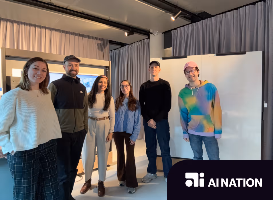 Group of six people standing side by side in a modern room with curtains and screens, with AI Nation logo in the bottom right corner.