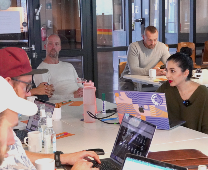 People collaborating around a table with laptops and drinks in a modern office space.