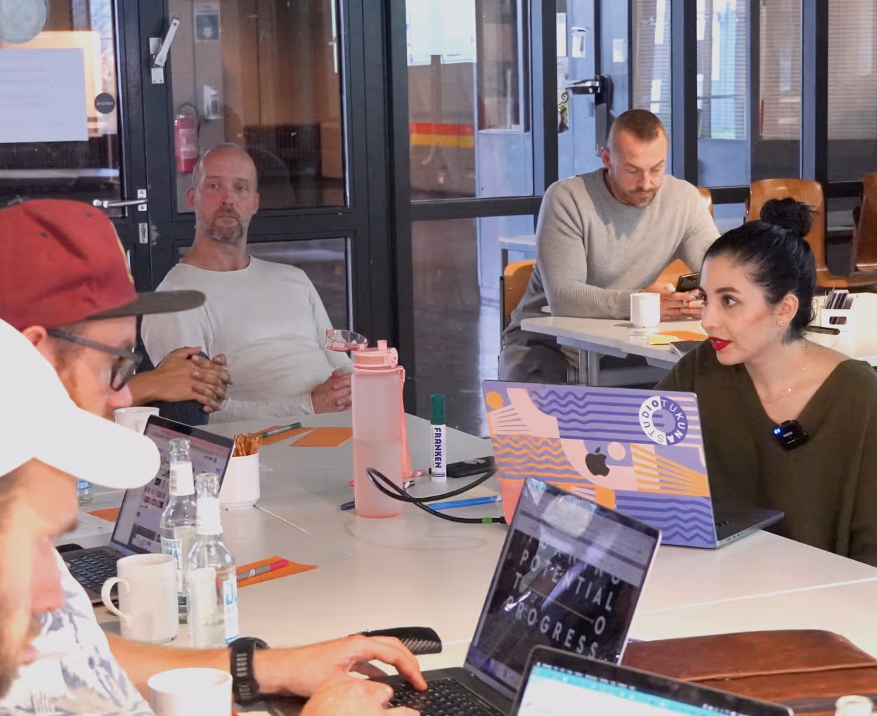 People collaborating around a table with laptops and drinks in a modern office space.