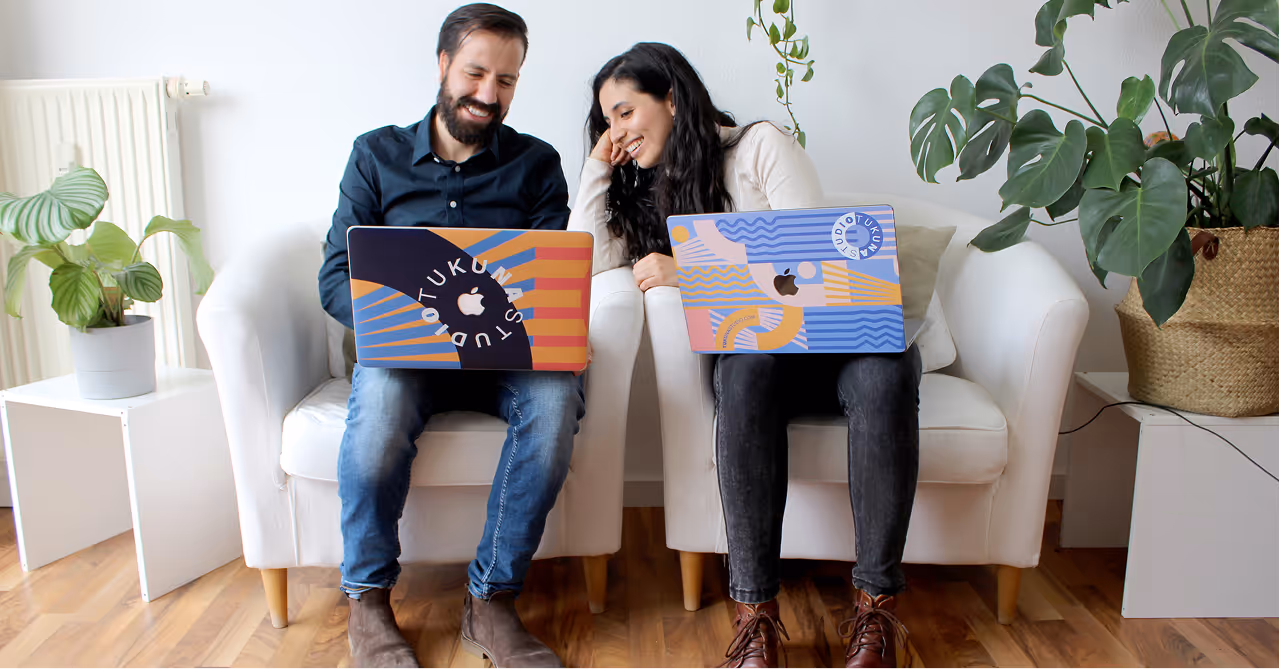 Man and woman sitting on white chairs with decorated laptops, smiling and looking at the screens.
