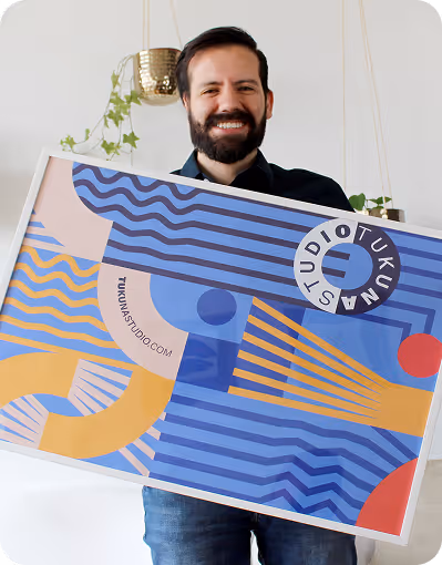 Smiling bearded man holding colorful abstract art print with geometric shapes and text 'tukunstudio.com'.