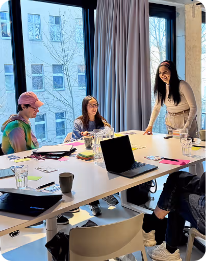 Three people collaborating in a bright meeting room with a laptop and notes on the table.