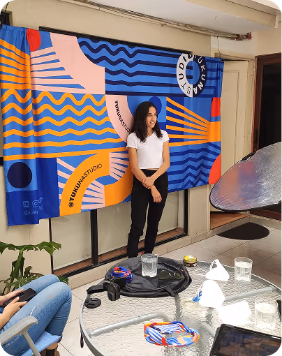 Young woman in white shirt and black pants posing in front of a colorful blue and orange patterned backdrop indoors.