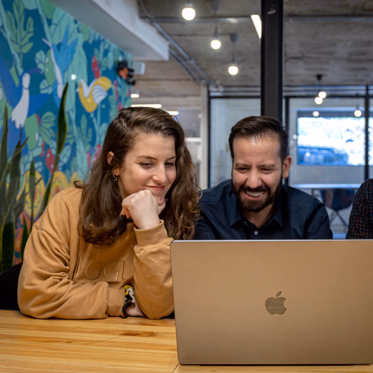 Two team members smiling while working together on a laptop in an office.
