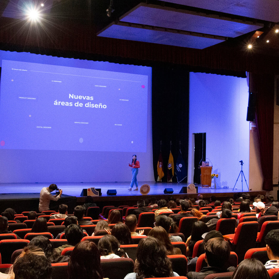 Audience watches a speaker on stage presenting a slide titled 'Nuevas áreas de diseño' in a large auditorium.
