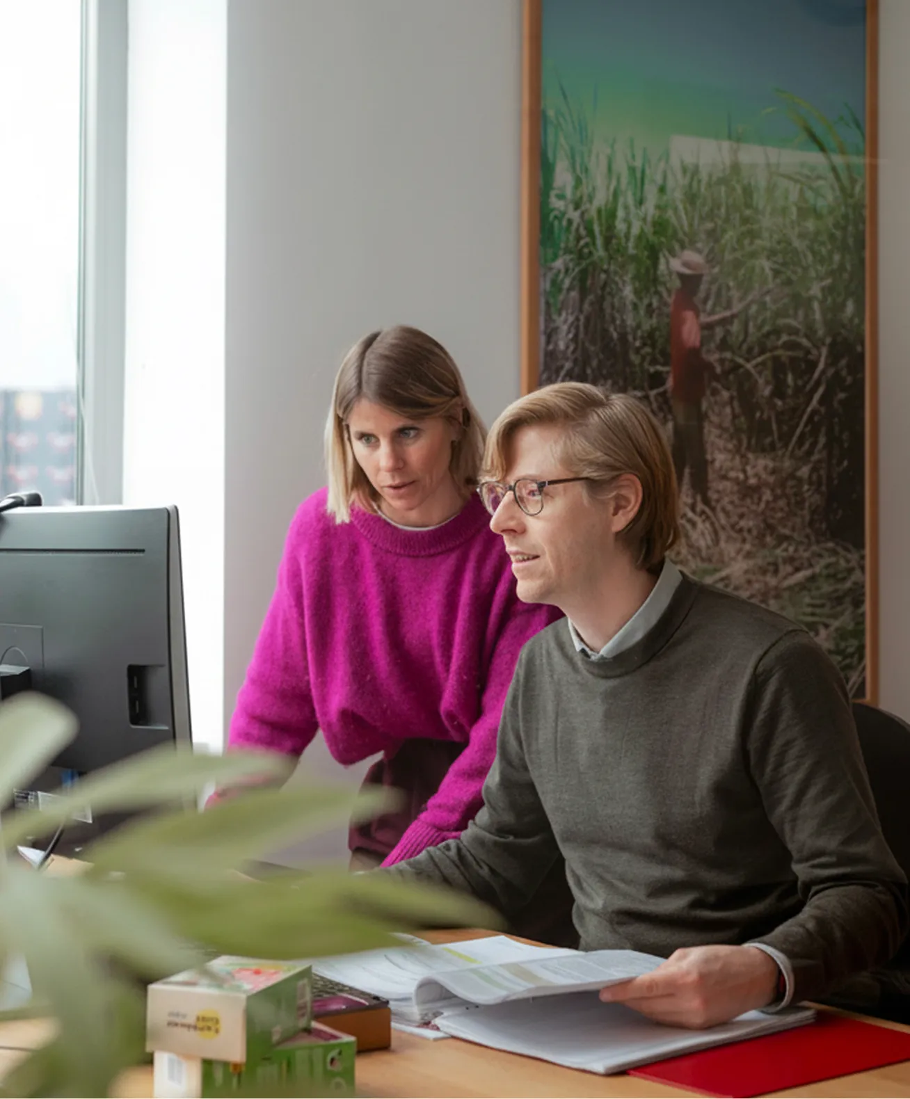Twee collega's van Caribbean Gold bespreken documenten terwijl ze naar een computerscherm kijken in een kantoor.
