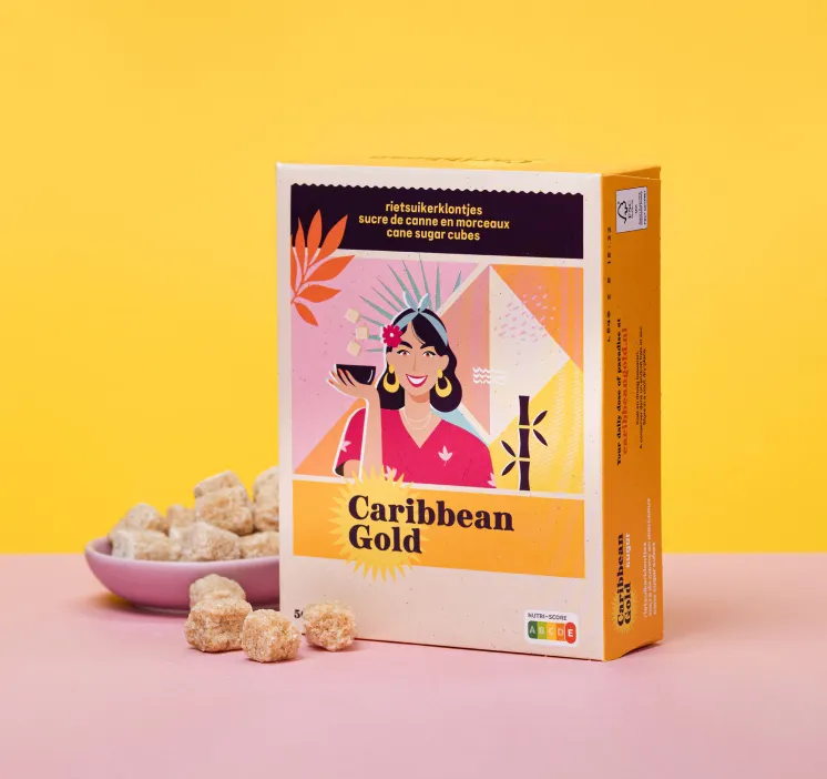 Verpakking Caribbean Gold met onregelmatige bruine rietsuikerklontjes en een roze kom met suikerklontjes op een roze oppervlak tegen een gele achtergrond.