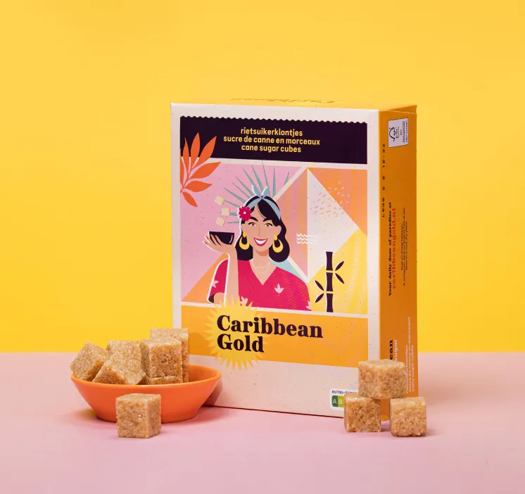 Pak Caribbean Gold rietsuikerklontjes naast een oranje schaaltje met suikerklontjes op een roze oppervlak en gele achtergrond.