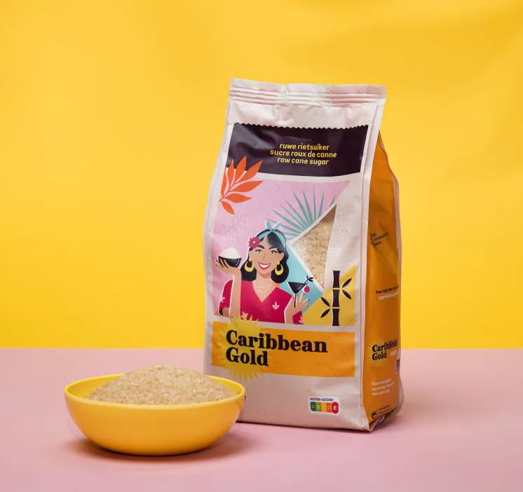 Zak Caribbean Gold ruwe rietsuiker met afbeelding van vrouw en een gele kom met suikerkorrels op roze en gele achtergrond.