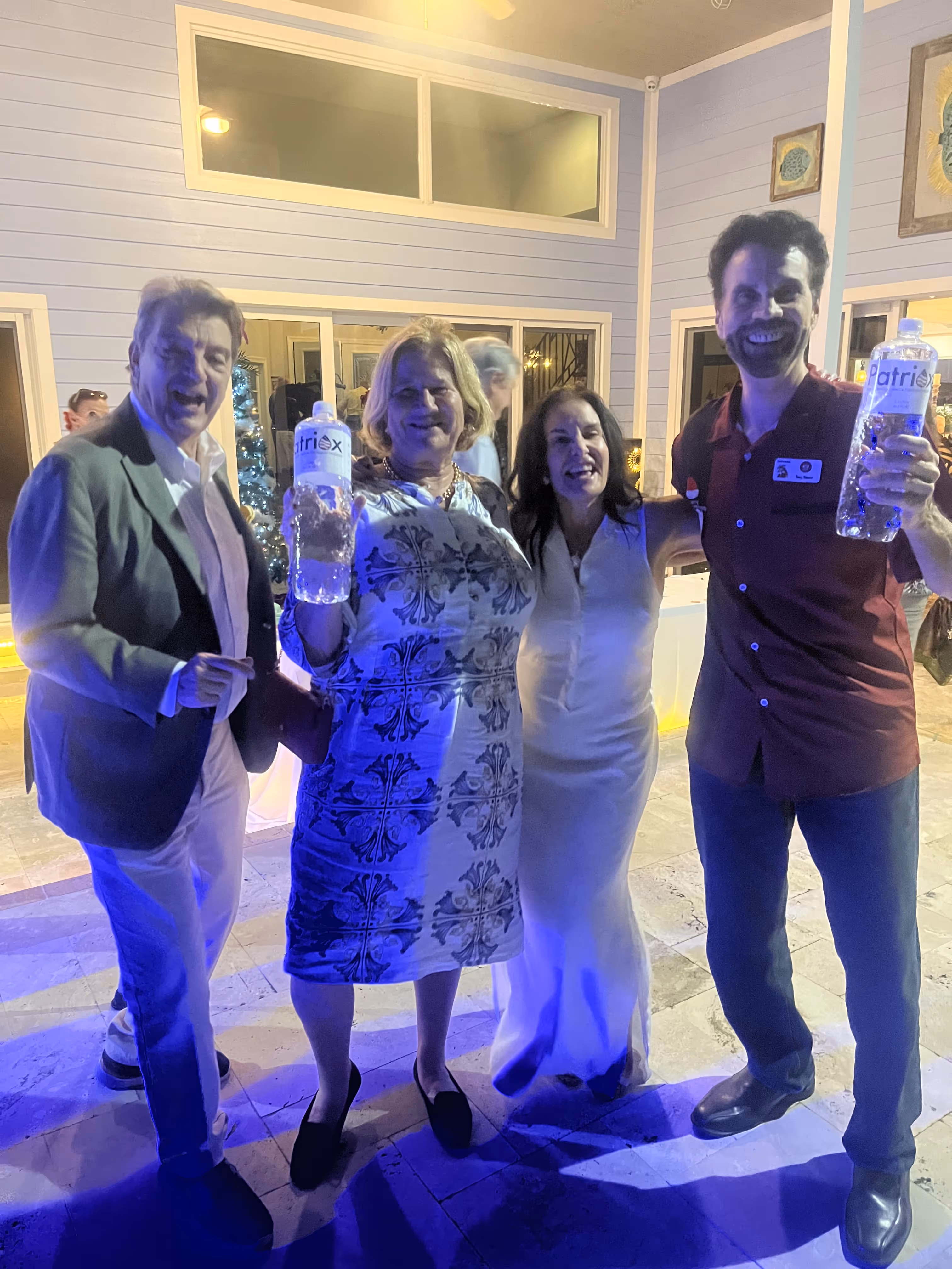 Four adults standing together indoors, two holding large bottles of water, smiling under blue lighting.