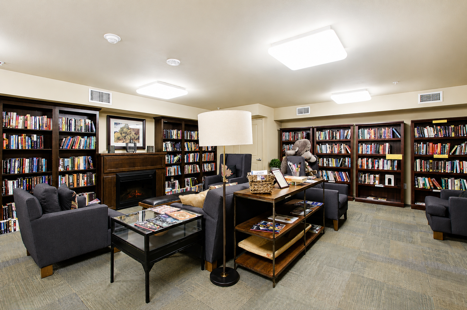 Cozy community library with fireplace, reading chairs, and extensive book collections offering a quiet retreat