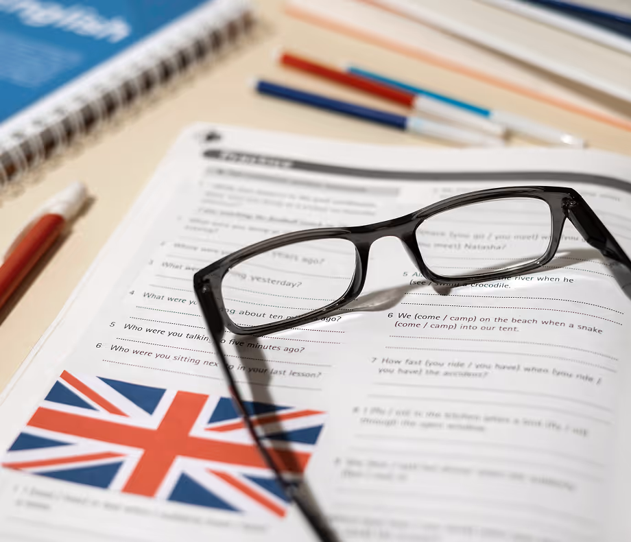 Black-framed eyeglasses resting on an English language workbook page featuring exercises and a Union Jack flag.