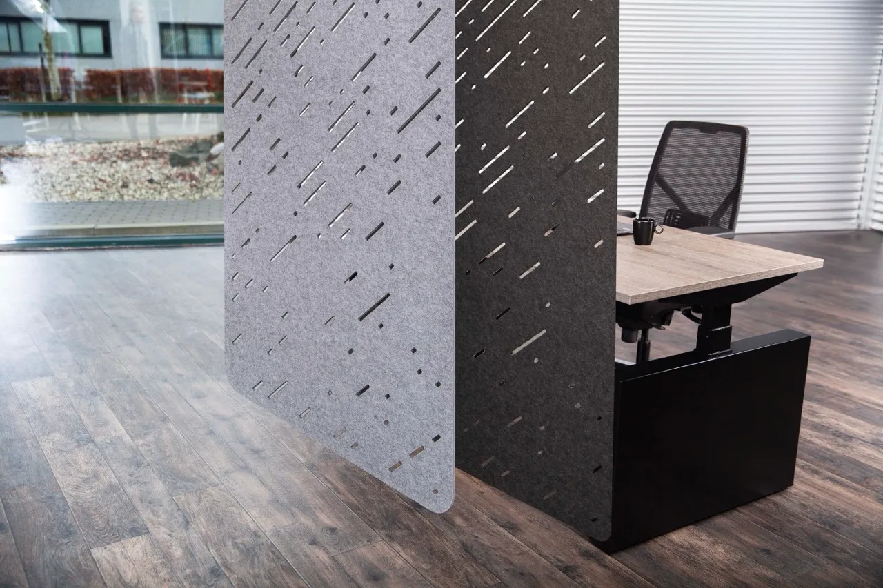 Modern bureau met een zwarte meshstoel en een koffiekopje, met decoratieve grijze en zwarte akoestische panelen ernaast, op een houten vloer.
