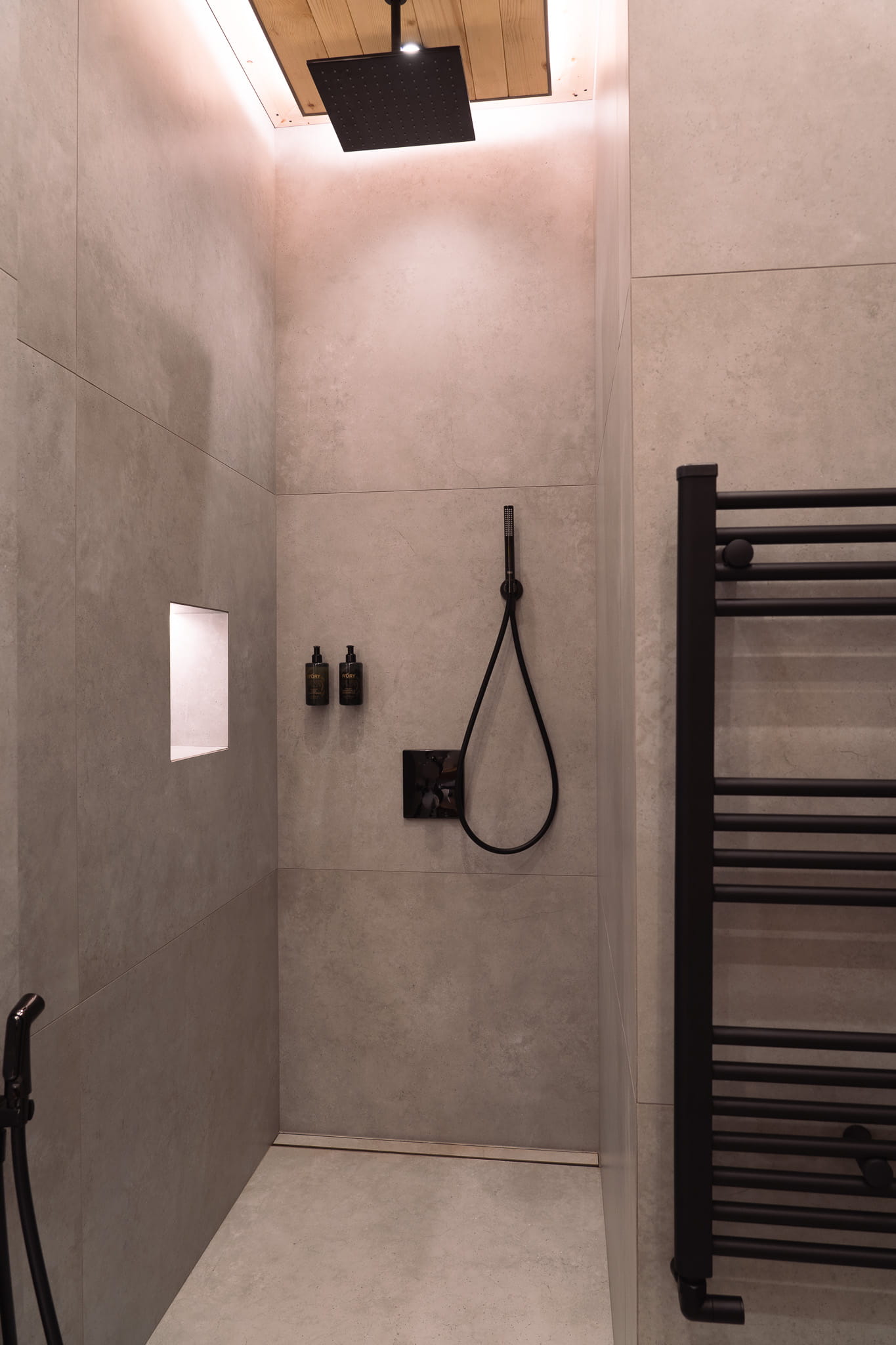 Modern shower with large overhead rain showerhead, handheld spray, and built-in niche in gray tiled walls.