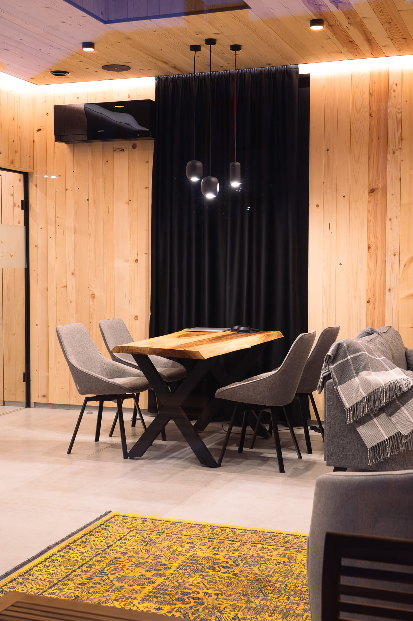 Modern dining area with a wooden table, four gray chairs, pendant lights, and wood-paneled walls.
